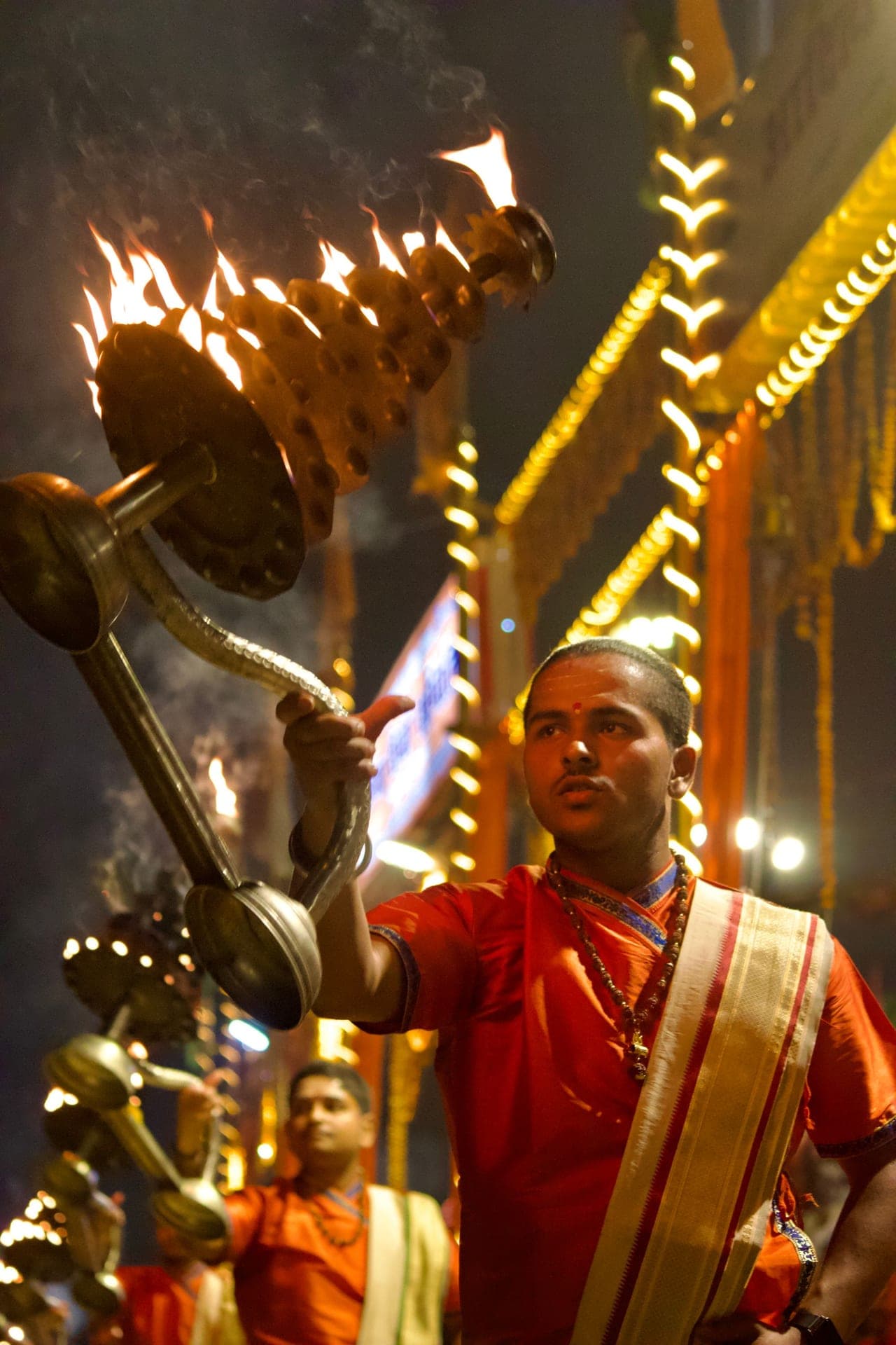 Ganga aarti in Varanasi, a priest raising a tiered brass lamp of flames into the night.