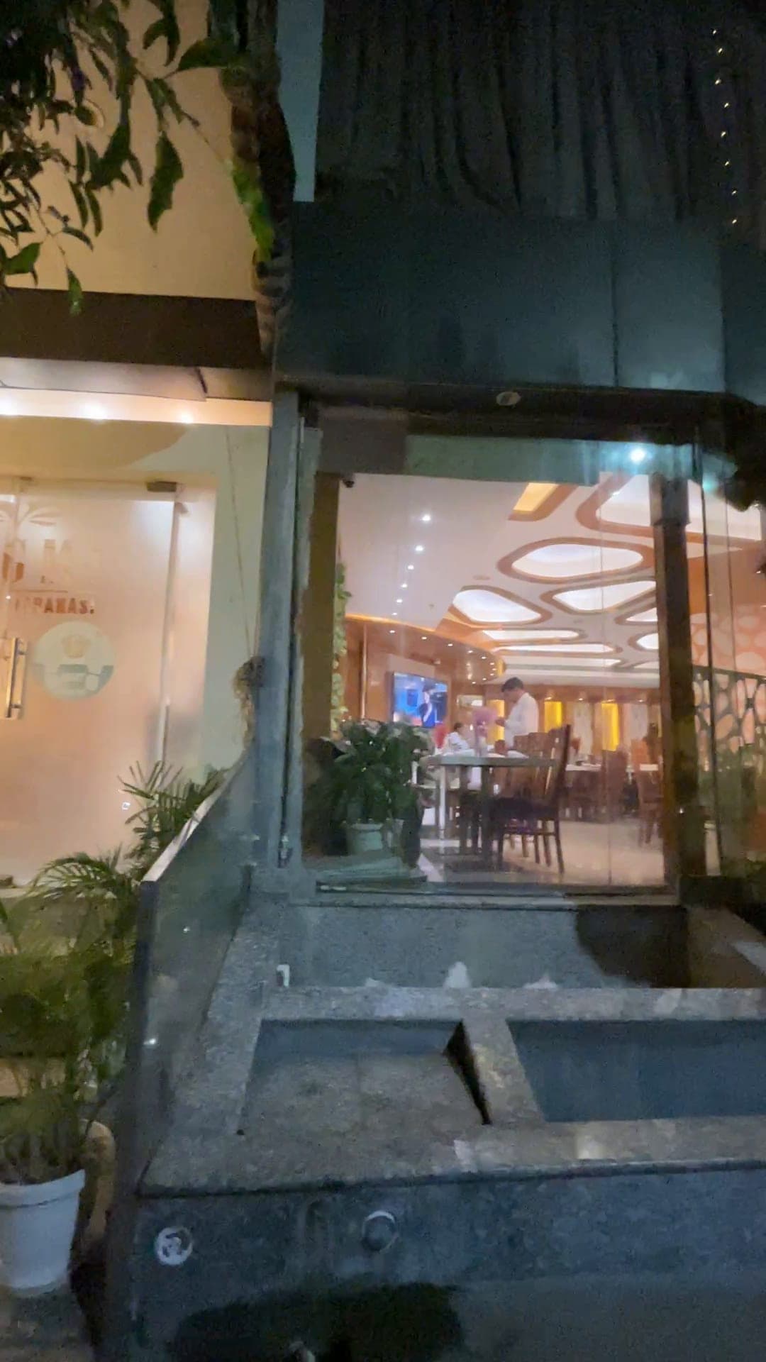 Hotel Vagmi lit at dusk — the glass frontage and the restaurant glowing within.