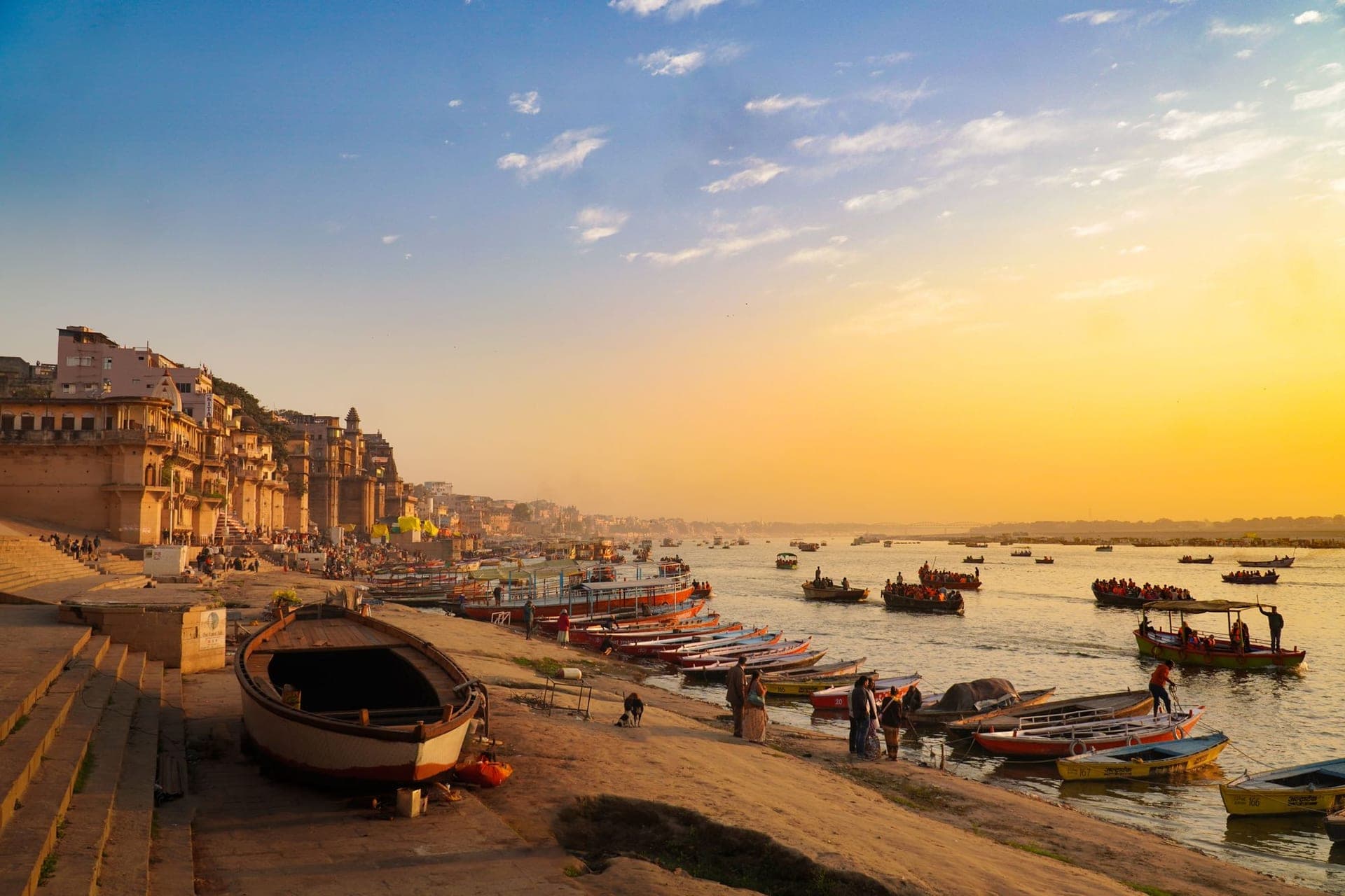The ghats of Varanasi at golden hour, wooden boats moored along the steps.