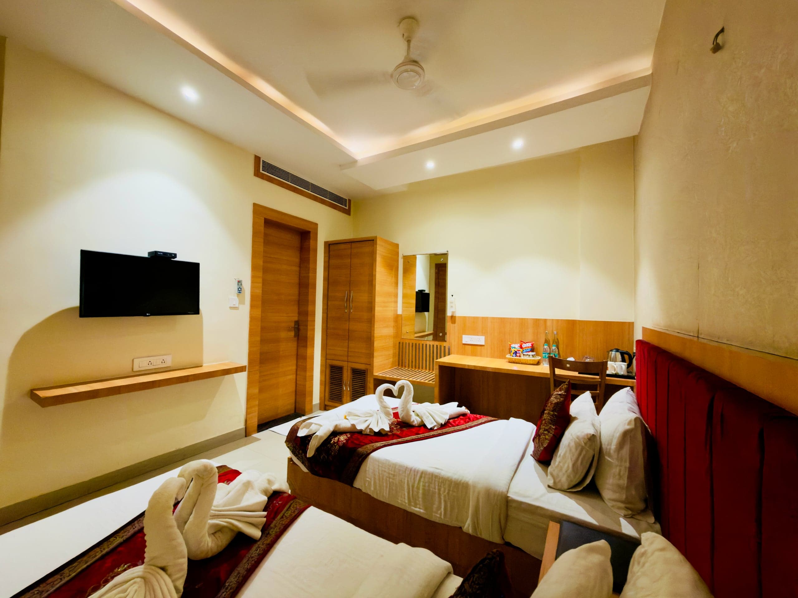 Deluxe room at Hotel Vagmi — king bed with deep-red velvet headboard, hand-folded towel swans, warm cove lighting