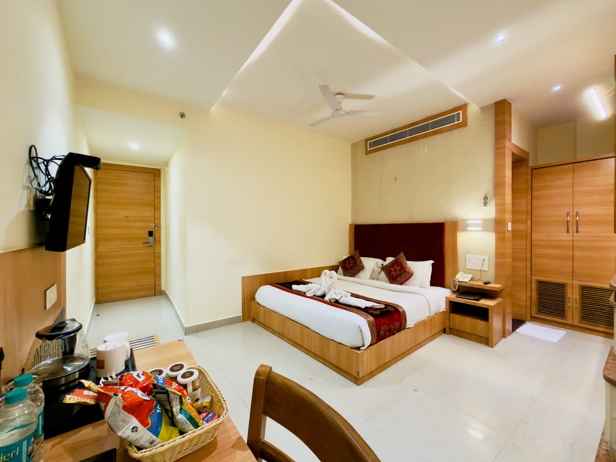Executive room at Hotel Vagmi — king bed with deep-red velvet headboard, entry hall and wardrobe in warm wood
