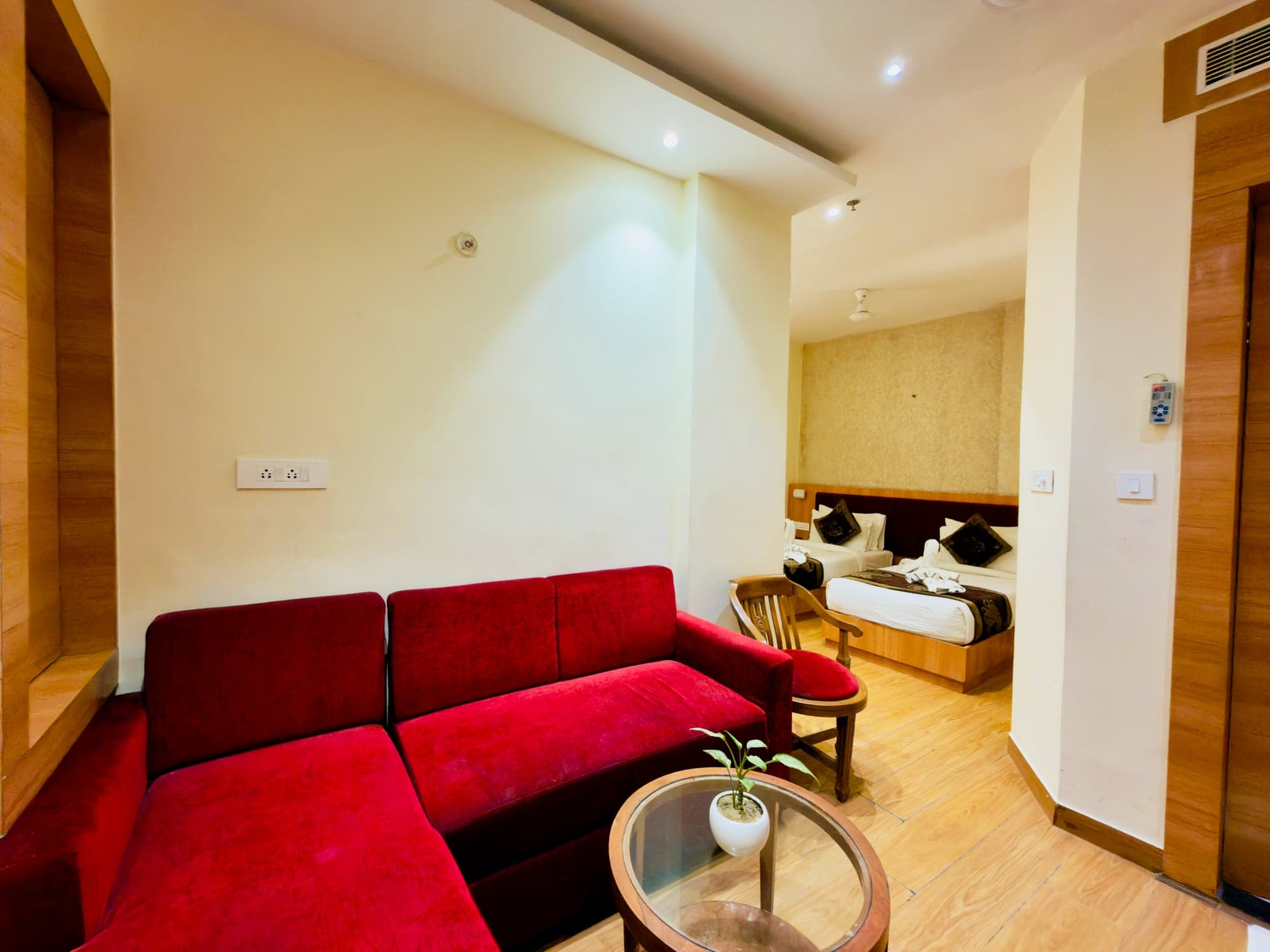 Mini Suite sitting room with a deep-red sofa, glass table and warm cove lighting