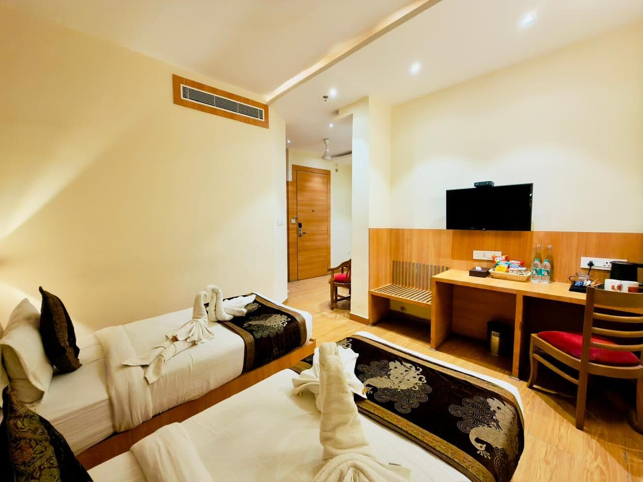 Mini Suite at Hotel Vagmi — warm wooden flooring, beds dressed in dark brocade runners, desk and wall-mounted TV